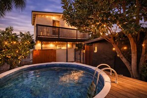 Ein zweistöckiges Gebäude mit Swimmingpool, Holzterrasse und Lichterketten.