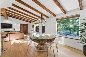 Ein modernes Interieur mit einem runden Glastisch, Holzbalken, einer Couch und einem großen Fenster.