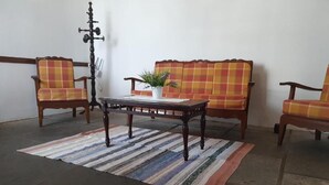 Een kamer met een houten bijzettafeltje, twee geruite fauteuils, een bank en een potplant.