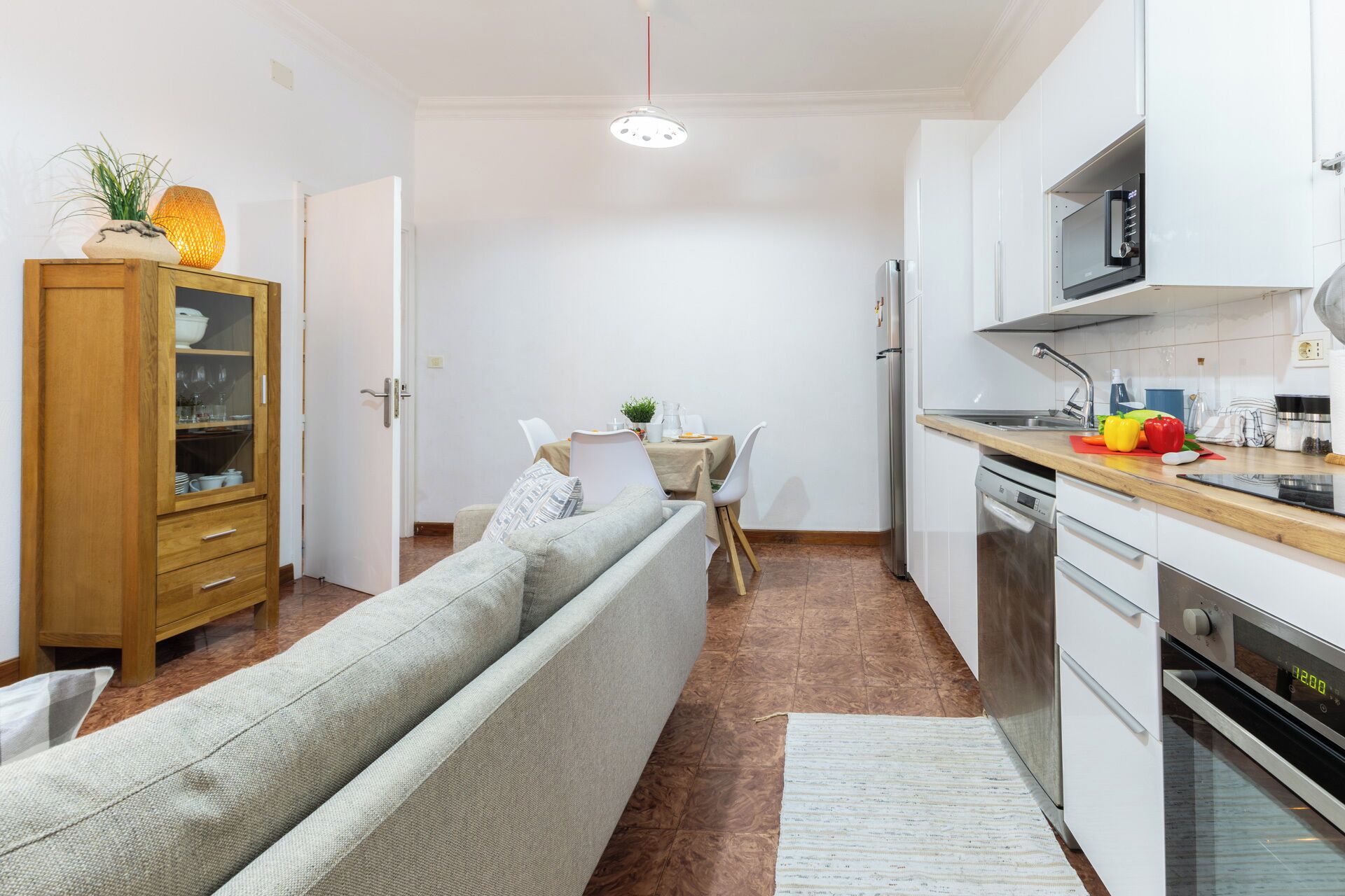 A compact kitchen with a microwave, oven, and dishwasher. There's a dining area with a table and chairs, and a sofa in the living area.