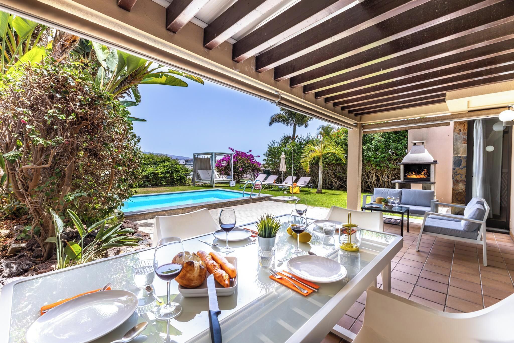Un área de comedor al aire libre con vista a la piscina, una parrilla y un espacio de estar cubierto.