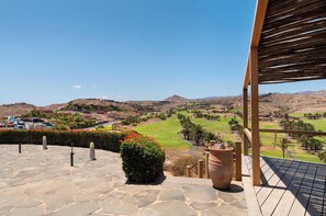 A stone-paved terrace with a view of a golf course, a wooden pergola, and a large planter.