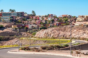 A hillside residential area with multi-story buildings, a curved road, and a landscaped area with yellow flowers.