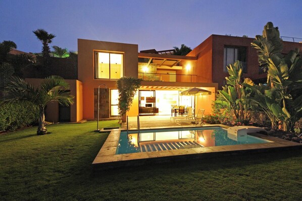 A modern house with a swimming pool, a patio with outdoor furniture, and a well-maintained garden.
