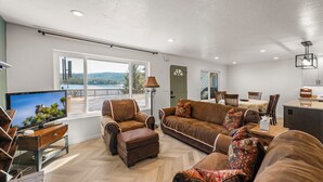 A spacious living area with a large window, a television, and a dining table. - Eads by the Lake (Fawnskin)