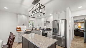 A modern kitchen with white cabinets, stainless steel appliances, and a marble island. - Eads by the Lake (Fawnskin)