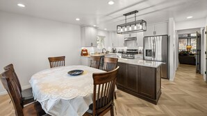 A modern kitchen with white cabinetry, a central island, and a dining area with a lace tablecloth. - Eads by the Lake (Fawnskin)