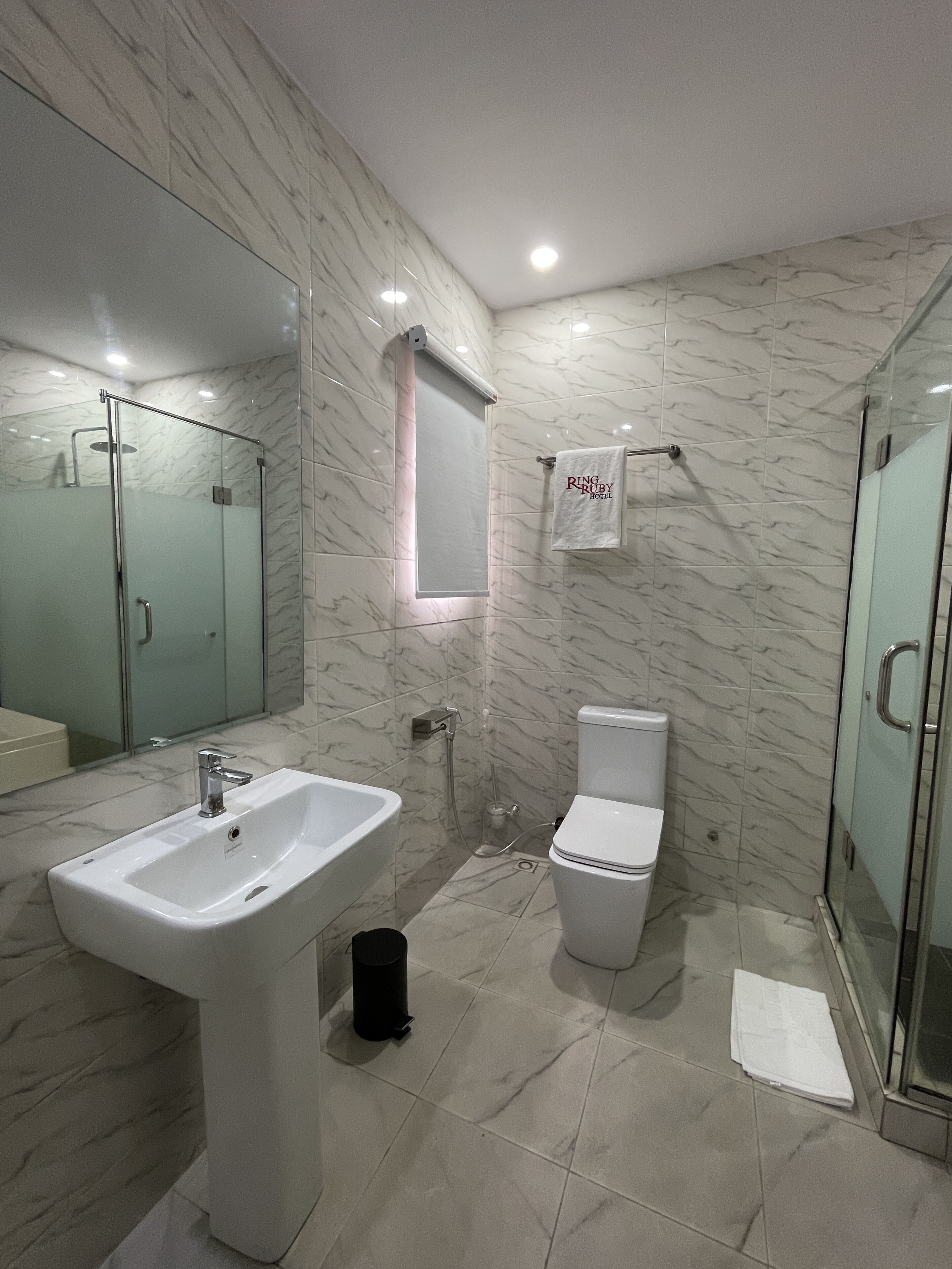 A modern bathroom with a marble floor, a white sink, a toilet, and a glass shower enclosure.