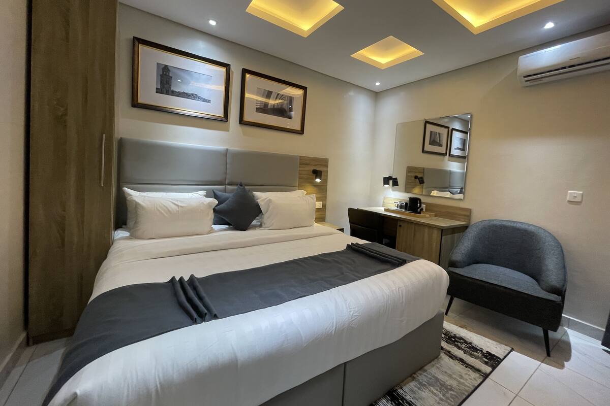 A modern hotel room with a bed, desk, chair, and a large mirror.