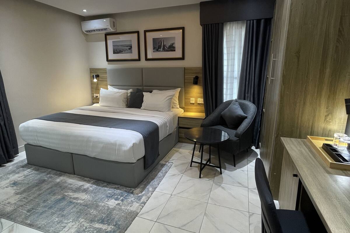 A modern hotel room with a large bed, a desk, a chair, and a small table.