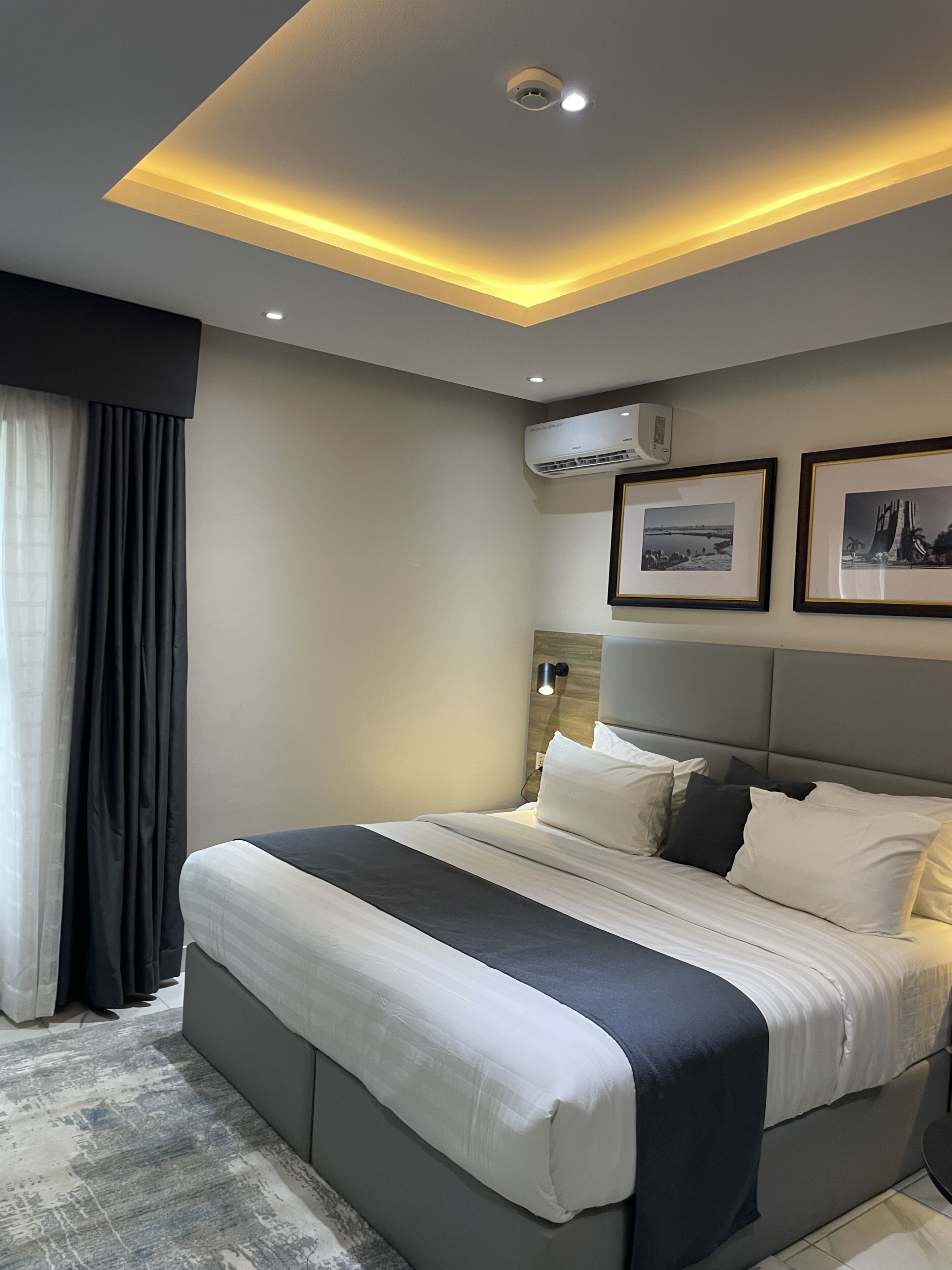 Una habitación de hotel moderna con una cama grande, una lámpara de techo, un equipo de aire acondicionado y cuadros en la pared.
