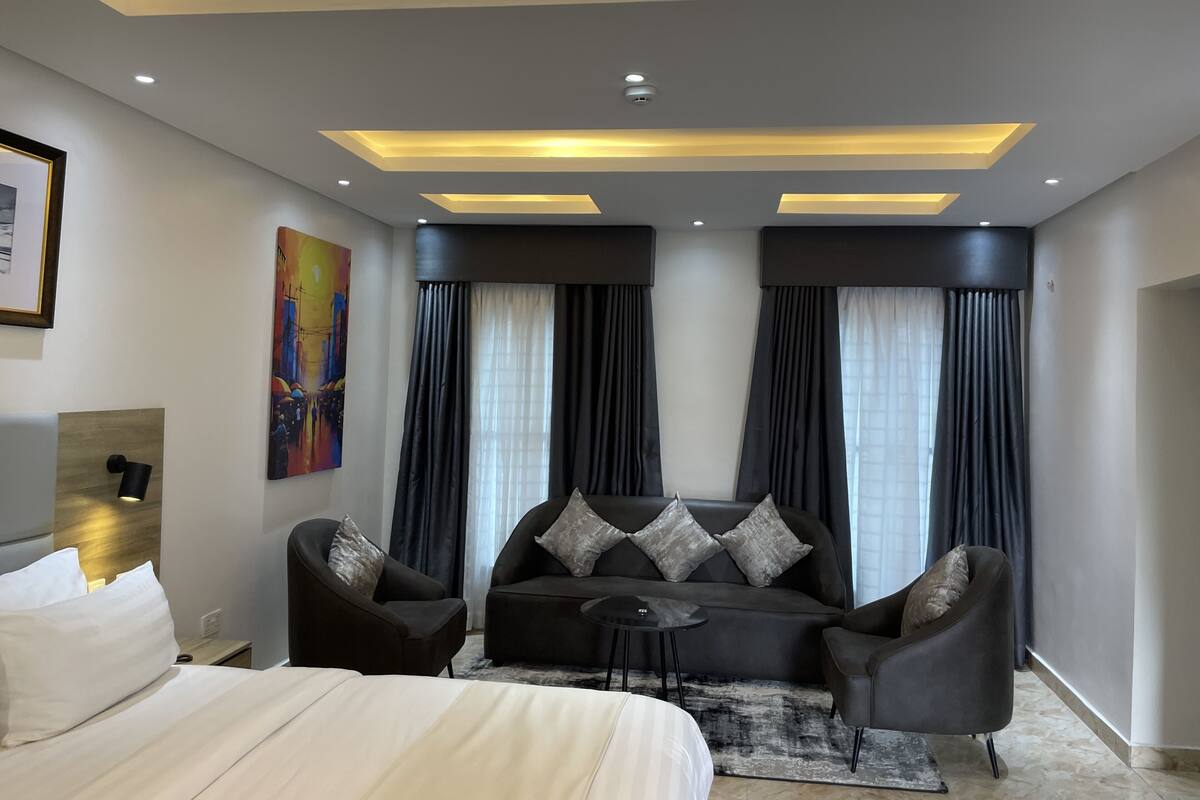 A modern hotel room with a bed, two armchairs, a sofa, a small table, and a painting on the wall.