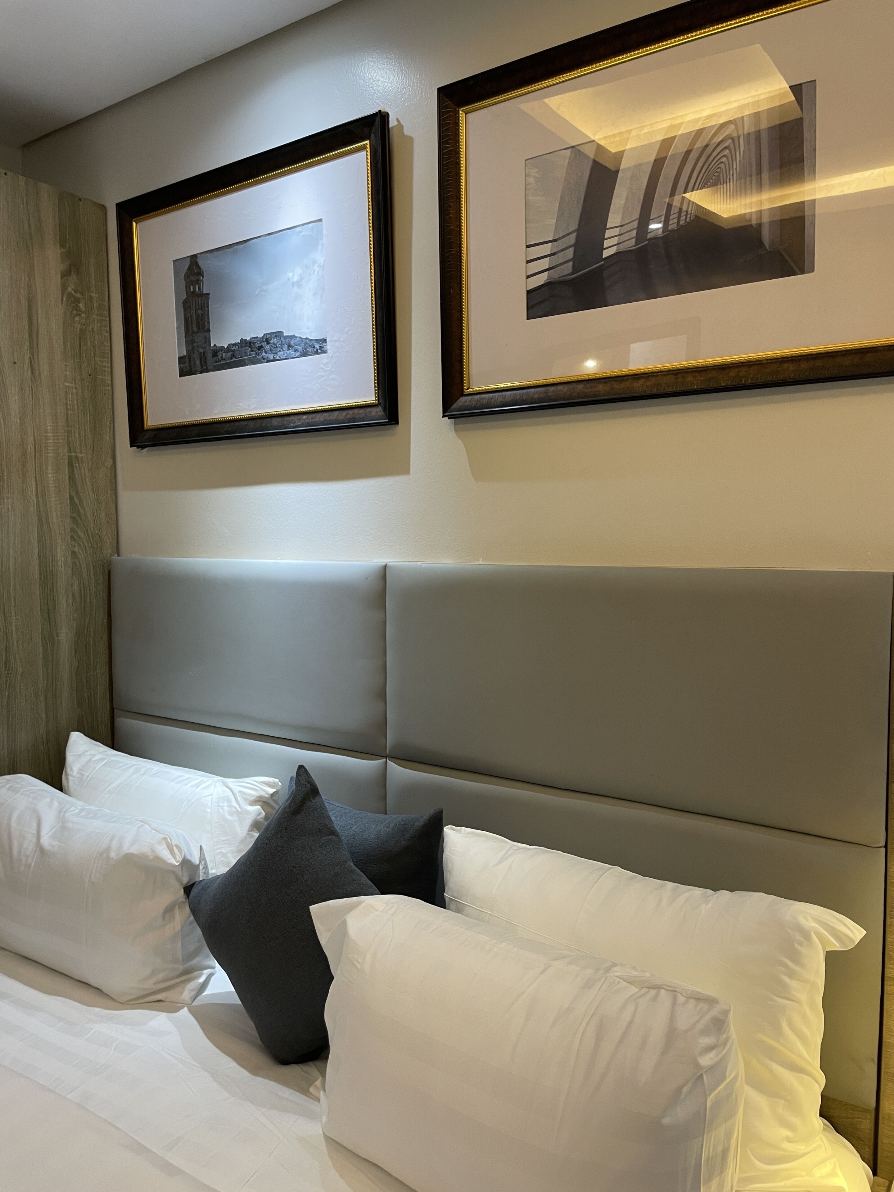A hotel room with a bed, pillows, and two framed pictures on the wall.