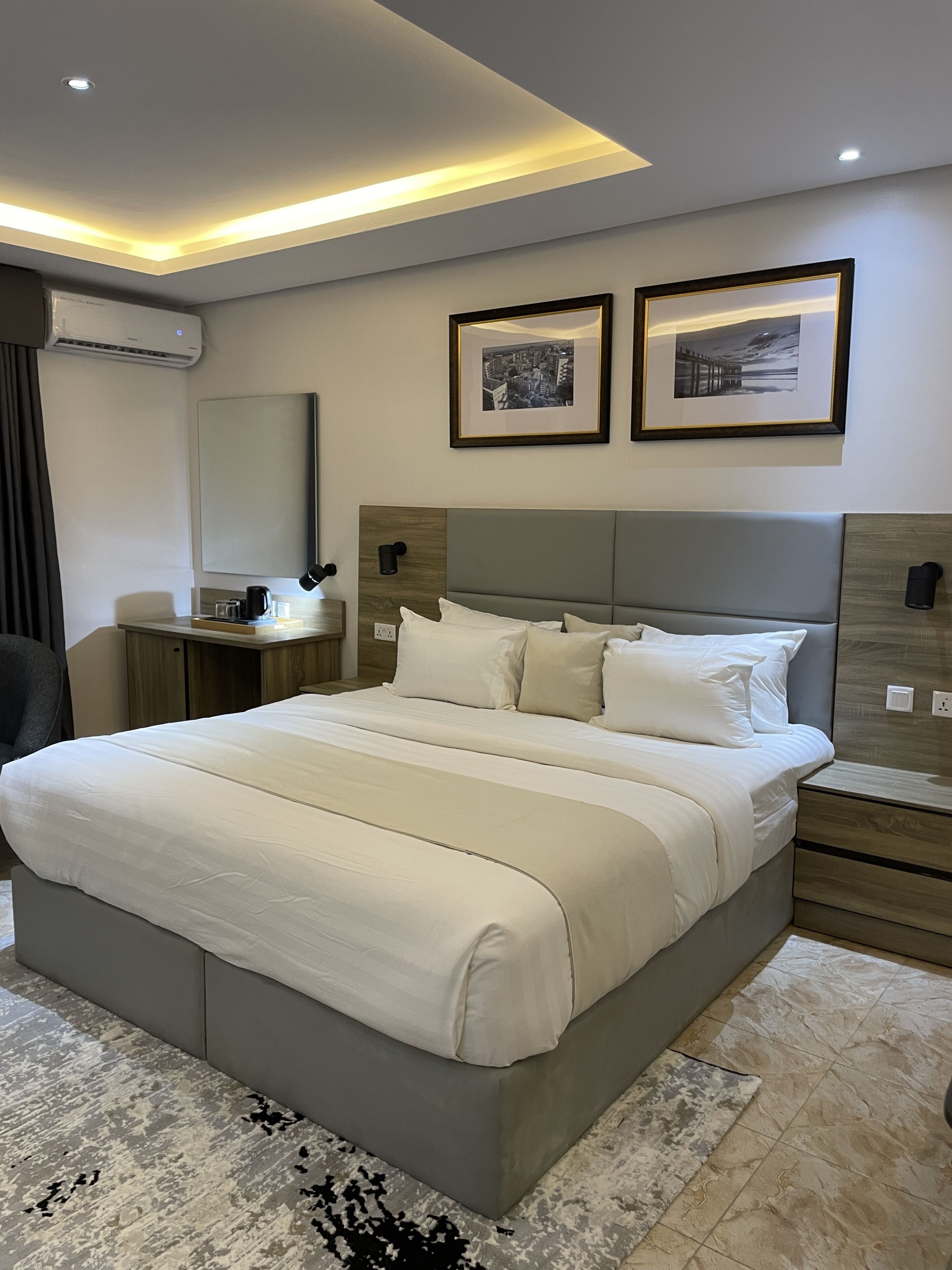 A modern hotel bedroom with a large bed, bedside tables, a desk, and a mirror.