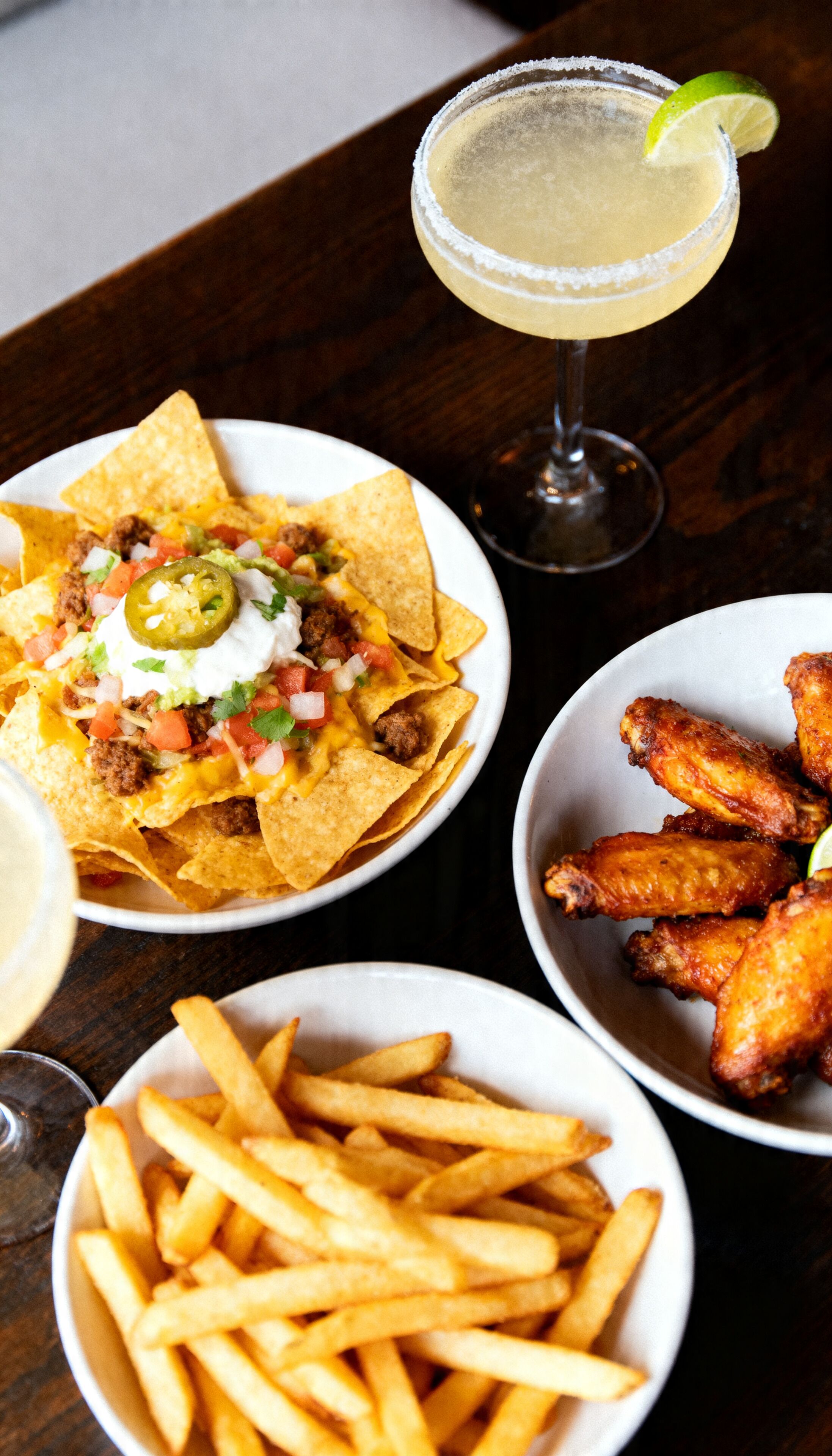 Nachos, wings, fries, and a margarita on a table.