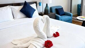 A hotel room with a neatly made bed, a blue armchair, a small table with a lamp, and a mirror on the wall. - SOMA Dream Hotel  (Georgetown)