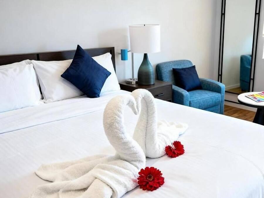 Une chambre d’hôtel avec un lit bien fait, un fauteuil bleu, une petite table avec une lampe et un miroir au mur.