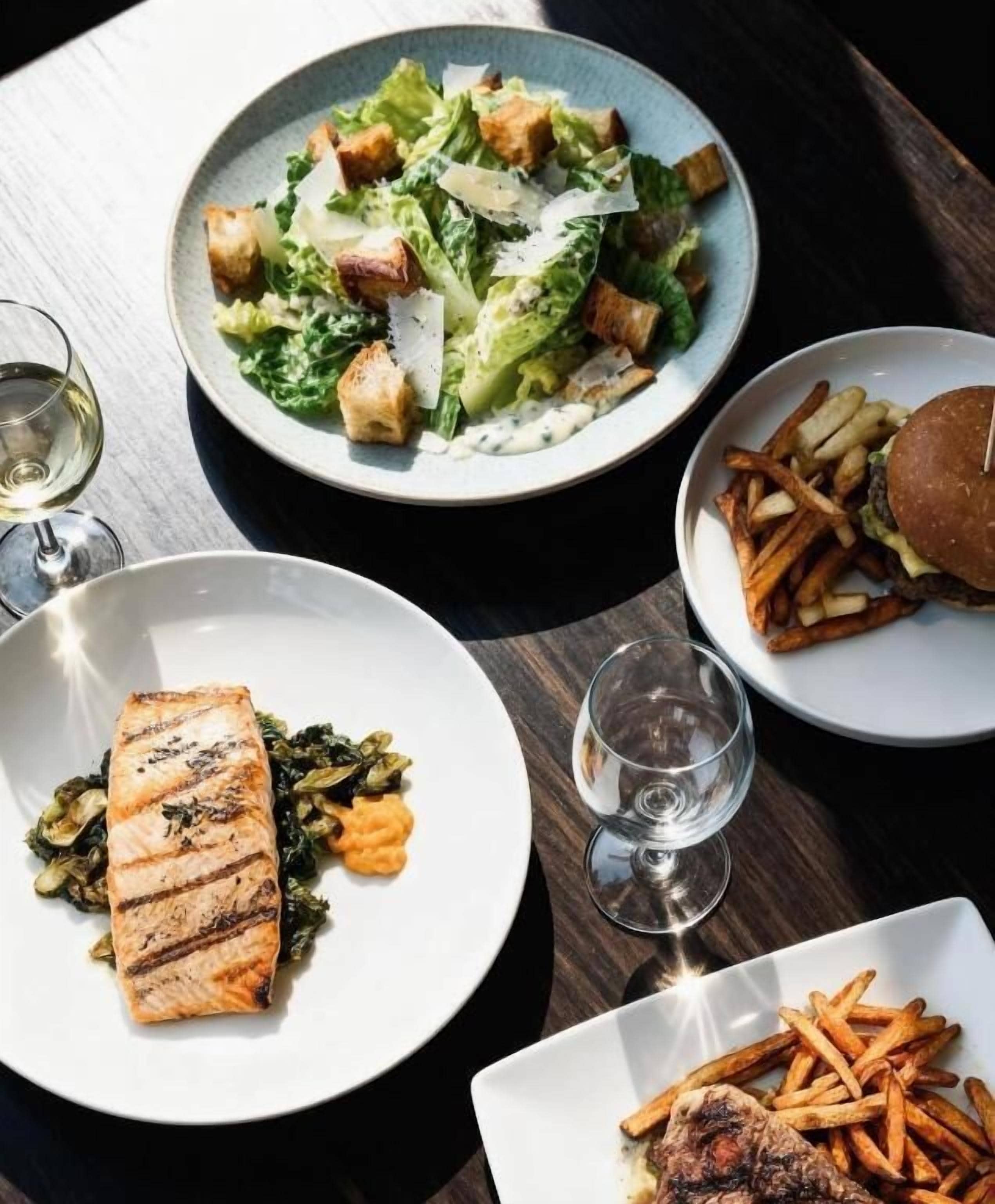 A table with various dishes including a salad, grilled salmon, a burger, and fries.
