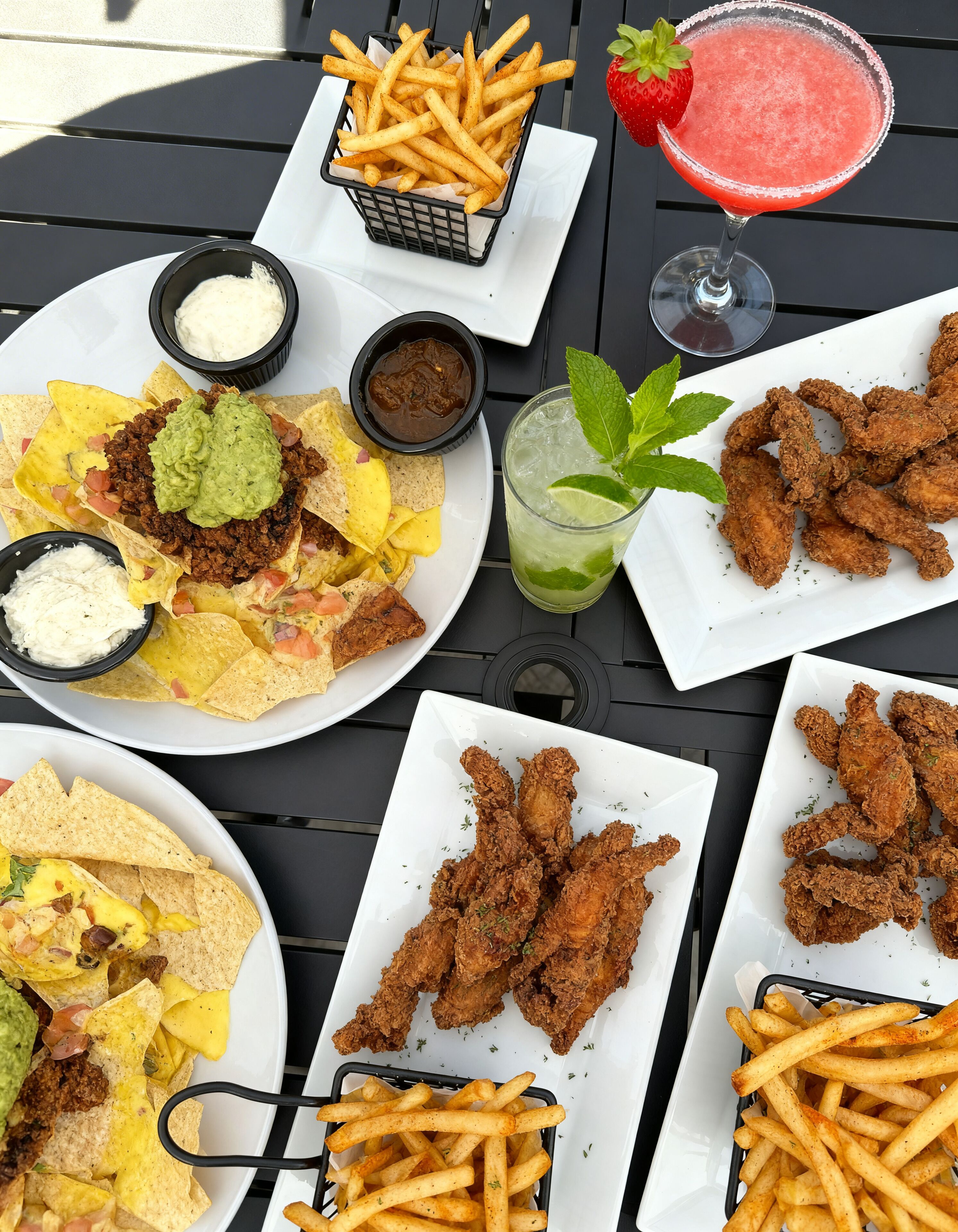 Una mesa con nachos, pollo frito, papas fritas y una margarita.