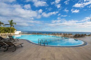 Ein Pool mit Liegestühlen, strahlend blauer Himmel und Blick auf den Ozean.