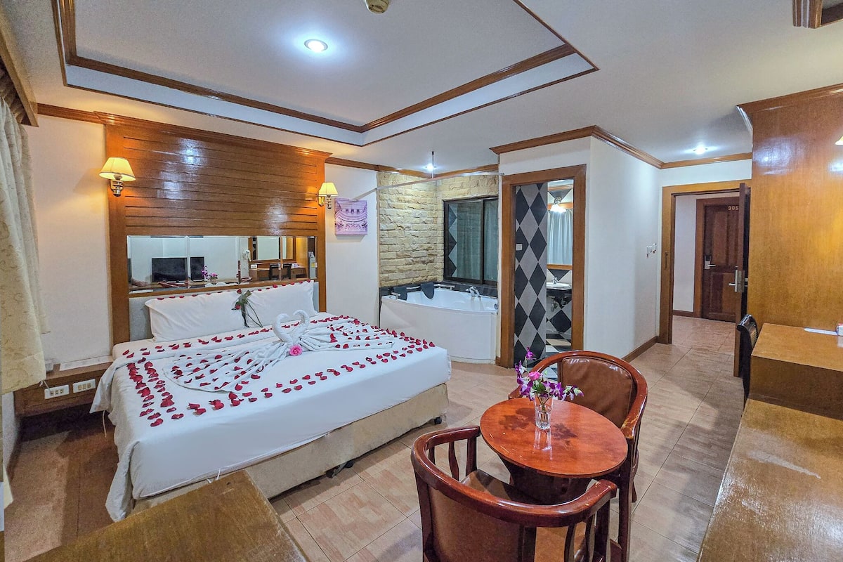 A hotel room with a bed, a bathroom, a dining table, and a mirror.