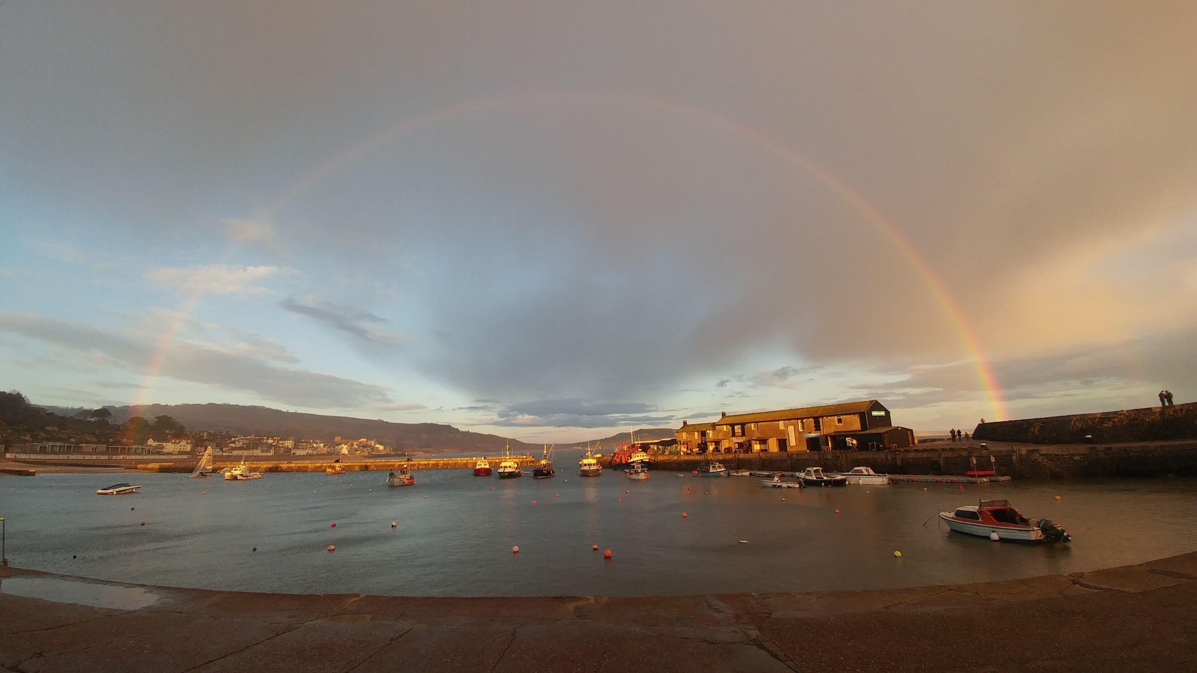 Un port avec des bateaux, un bâtiment et un arc-en-ciel.