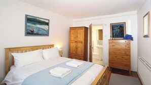 A bedroom with a bed, a wooden wardrobe, a bathroom visible through an open door, and a painting on the wall. - Blue Horizons seaside flat in town centre (Lyme Regis)