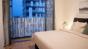 Ein Schlafzimmer mit einem Bett, einer Topfpflanze und Blick auf ein Gebäude durch eine Glasdoor.