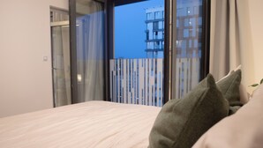 Ein Schlafzimmer mit einem Bett, einem Fenster mit Vorhängen und Blick auf ein Gebäude.