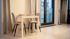 Ein moderner Essbereich mit einem weißen Tisch und Stühlen, einem Weinglas und Blick auf einen Balkon.