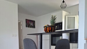 Une cuisine moderne avec deux tabourets de bar, un panier de fruits posé sur le comptoir et un luminaire suspendu.