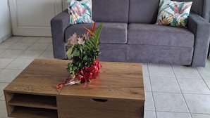 Un salon avec un canapé gris, une table basse en bois agrémentée d’un arrangement floral et une porte blanche.
