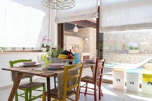 Un coin repas avec une table dressée pour quatre personnes, des chaises, un panier de fruits et une vue sur l’extérieur.