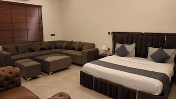 A modern bedroom with a sectional sofa, a large bed with a headboard, and a glass coffee table.