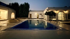 A swimming pool with a tiled deck, surrounded by buildings with arched windows and a door. - 2BR Villa with Pool, BBQ & Music at GoBravo Grandeur Gurgaon (Gurugram)