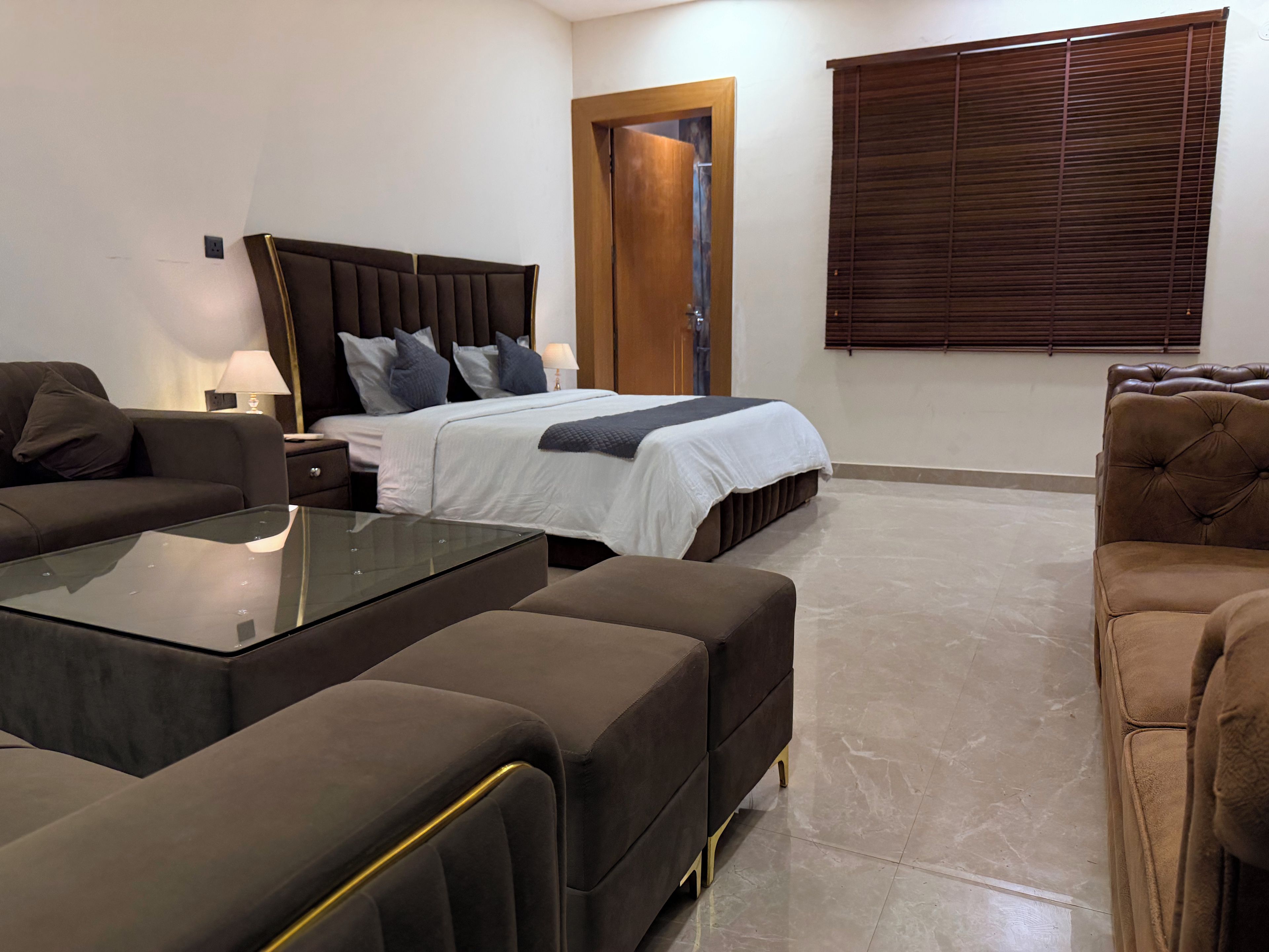 A modern bedroom with a large bed, a sofa, a glass coffee table, and a wooden door.