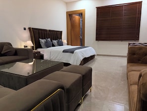 A modern bedroom with a large bed, a sofa, a glass coffee table, and a wooden door. - 2BR Villa with Pool, BBQ & Music at GoBravo Grandeur Gurgaon (Gurugram)