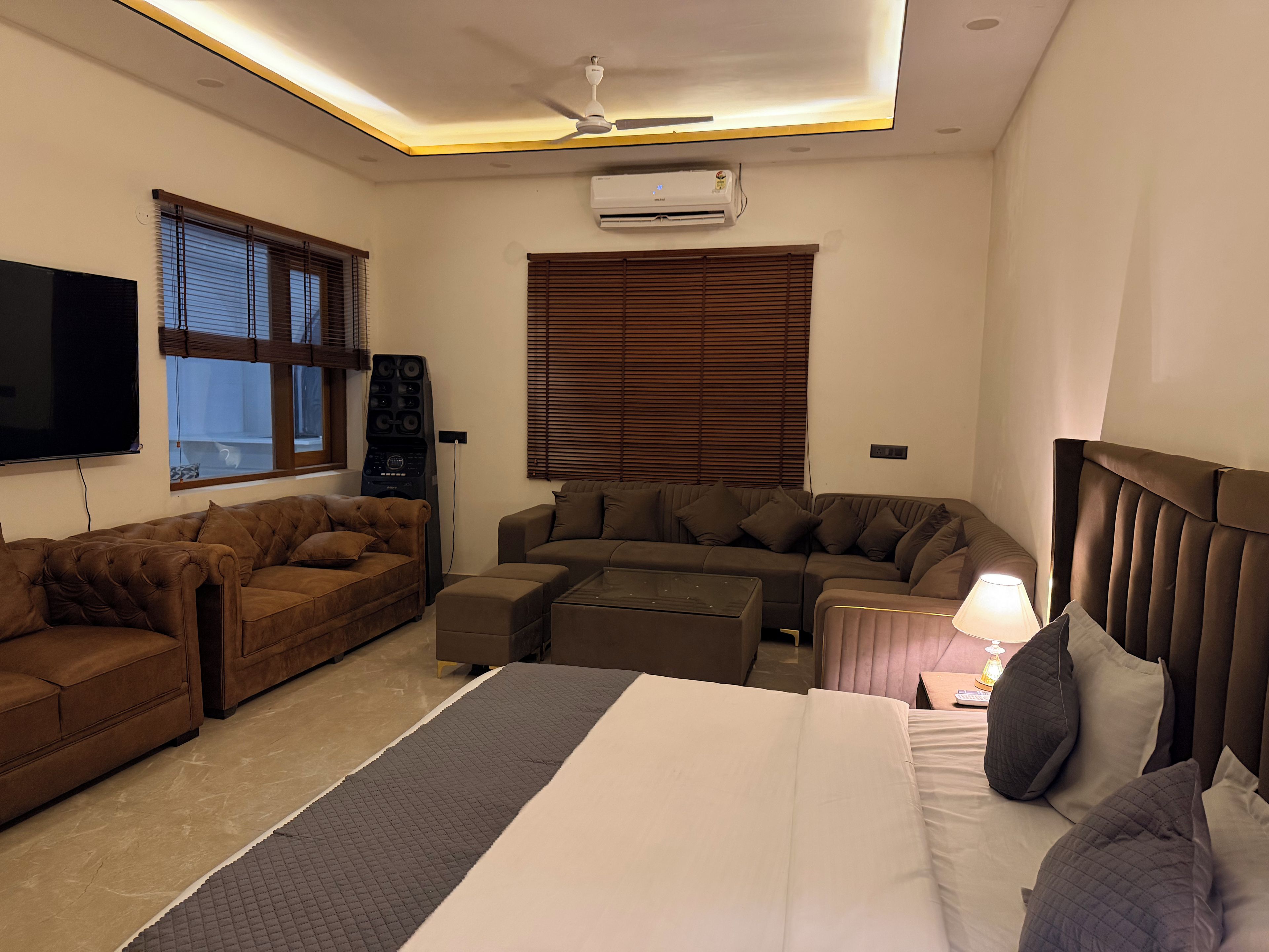 A hotel room with a bed, two sofas, a television, and an air conditioning unit.