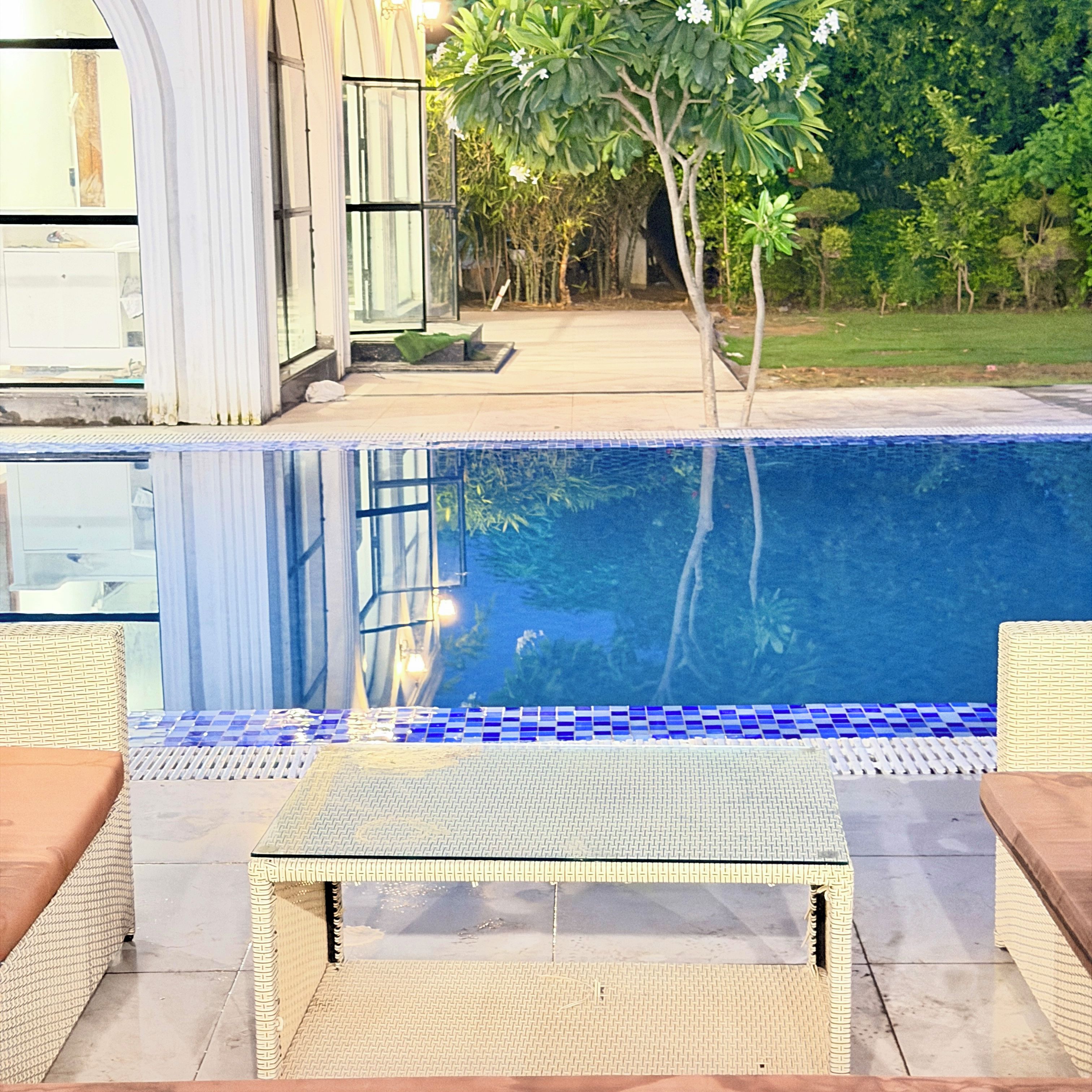 A swimming pool with a tiled edge, surrounded by a patio area with wicker furniture.