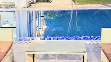 A swimming pool with a tiled edge, surrounded by a patio area with wicker furniture.