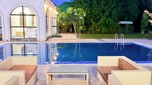 A swimming pool with lounge chairs, a building with arched windows, and a garden. - 2BR Villa with Pool, BBQ & Music at GoBravo Grandeur Gurgaon (Gurugram)