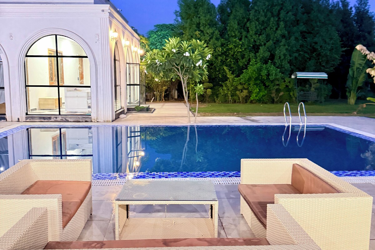 A swimming pool with lounge chairs, a building with arched windows, and a garden.