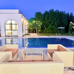 A swimming pool with lounge chairs, a building with arched windows, and a garden. - 2BR Villa with Pool, BBQ & Music at GoBravo Grandeur Gurgaon (Gurugram)