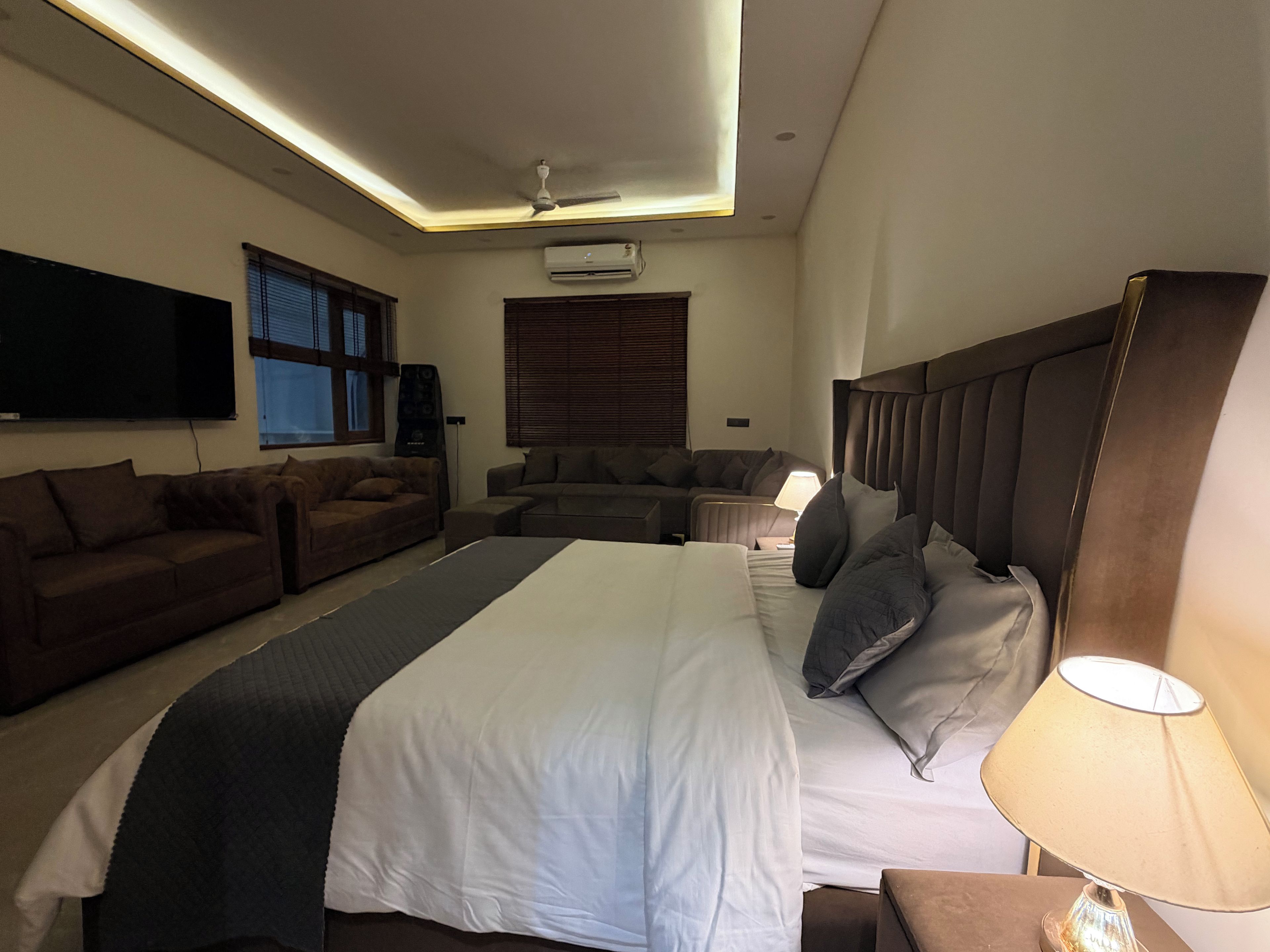 A modern hotel room with a large bed, a sofa, a flat-screen TV, and a ceiling fan.