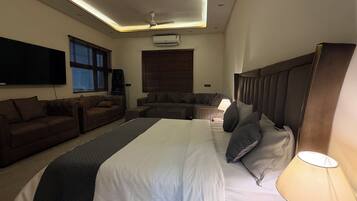 A modern hotel room with a large bed, a sofa, a flat-screen TV, and a ceiling fan.