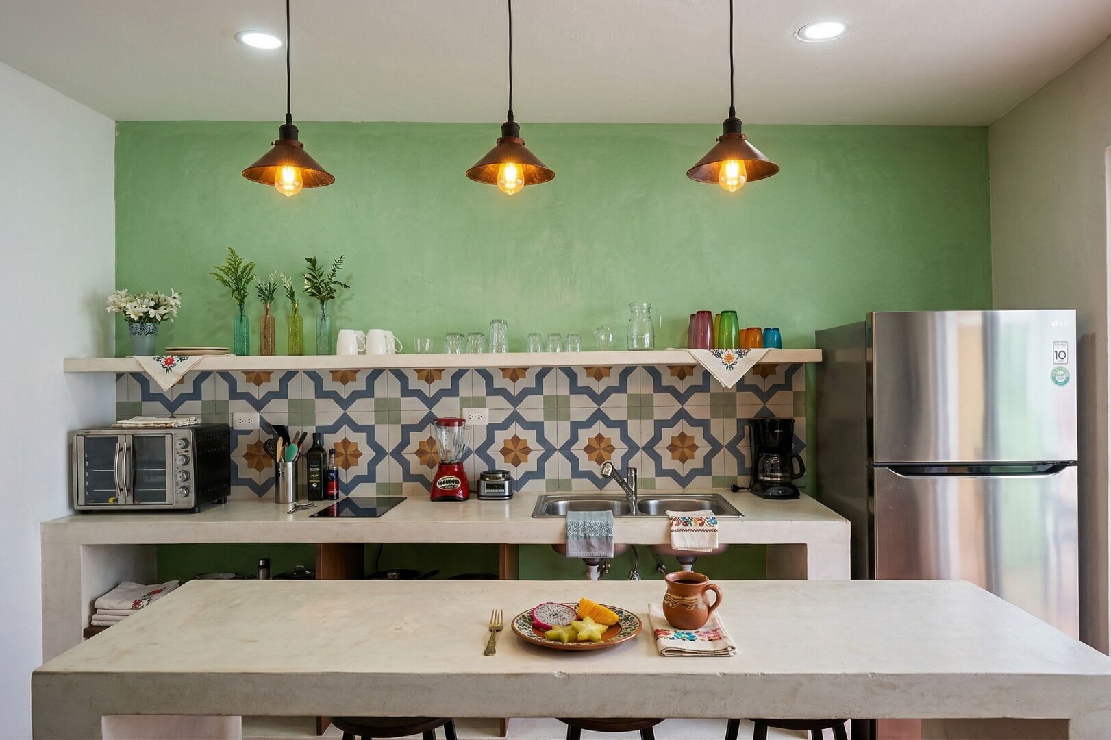 A kitchen with a green wall, three pendant lights, a stainless steel refrigerator, a toaster, and a coffee maker.