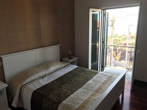 Un dormitorio con cama, mesita de noche, lámpara y puerta corrediza de vidrio que da a un balcón.