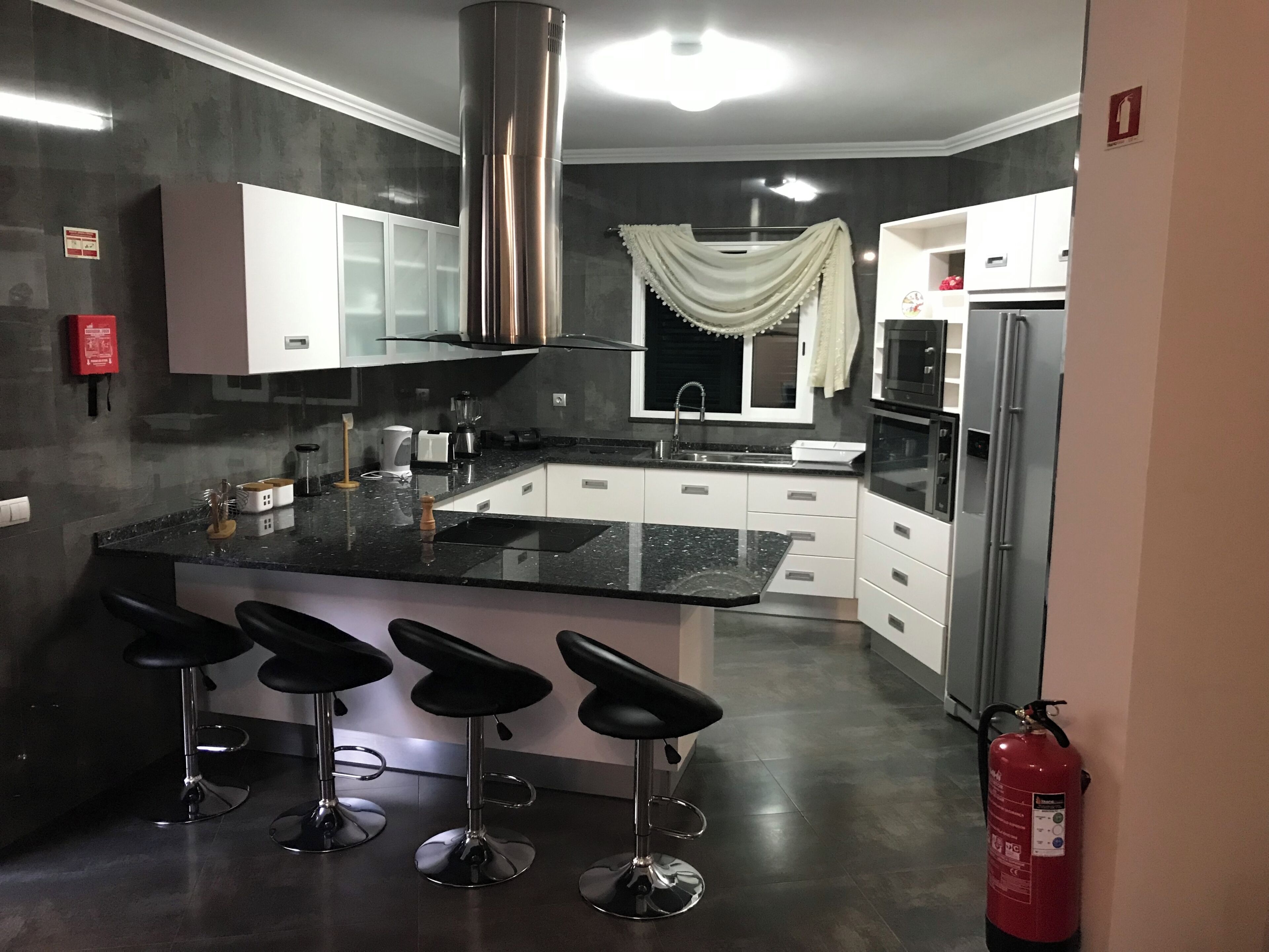 A modern kitchen with a black countertop, white cabinets, stainless steel appliances, and a fire extinguisher.