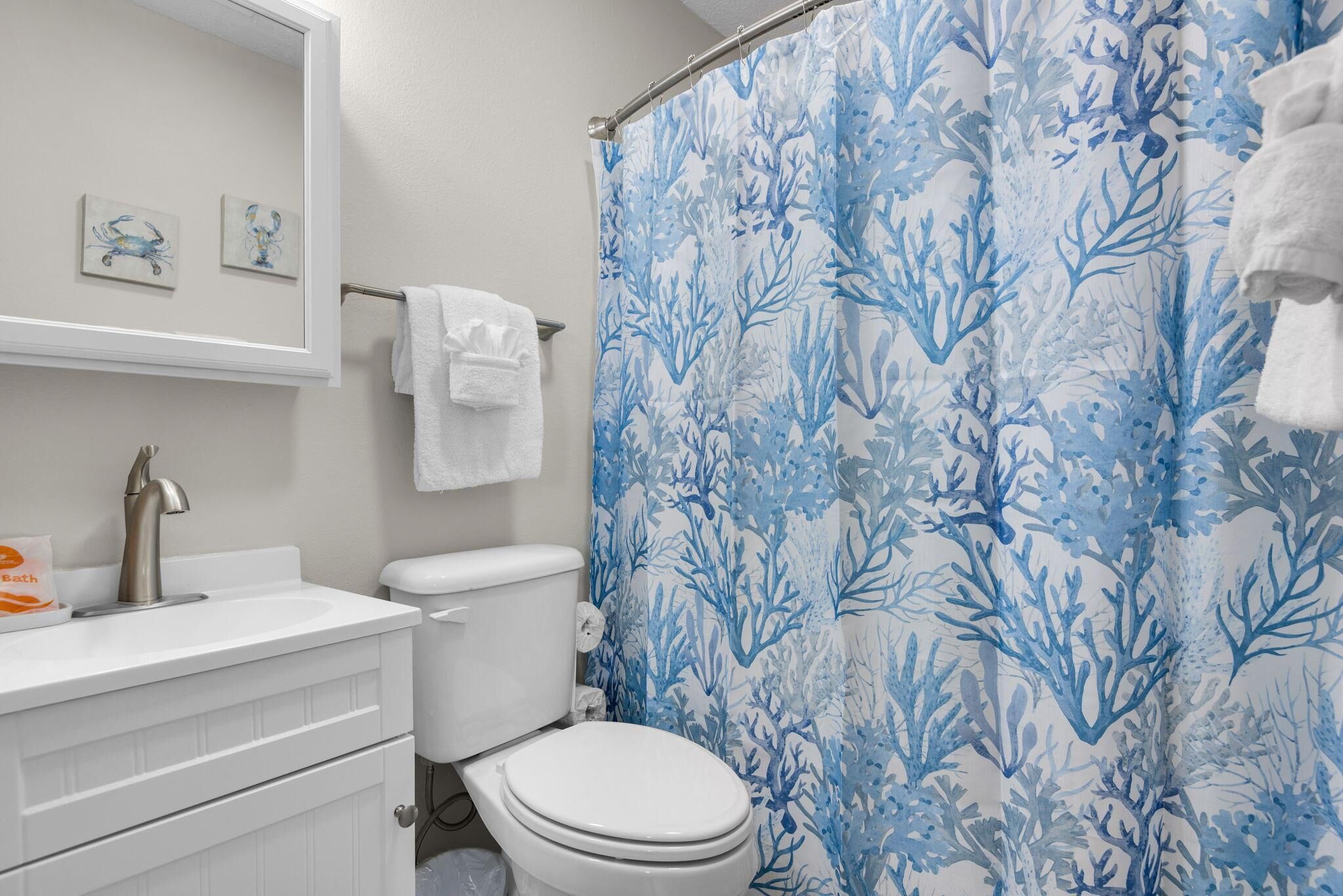 A bathroom with a white sink, a toilet, a shower curtain with a blue coral pattern, and a towel rack with a white towel.