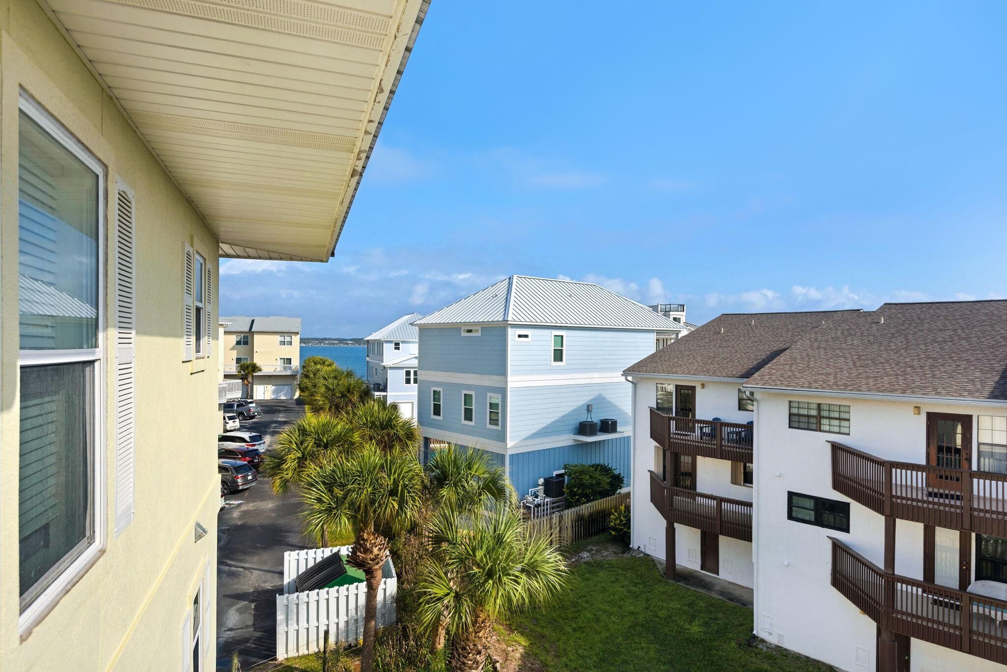 A residential area with a white building with a balcony, a blue building with a grey roof, and a view of the sea.